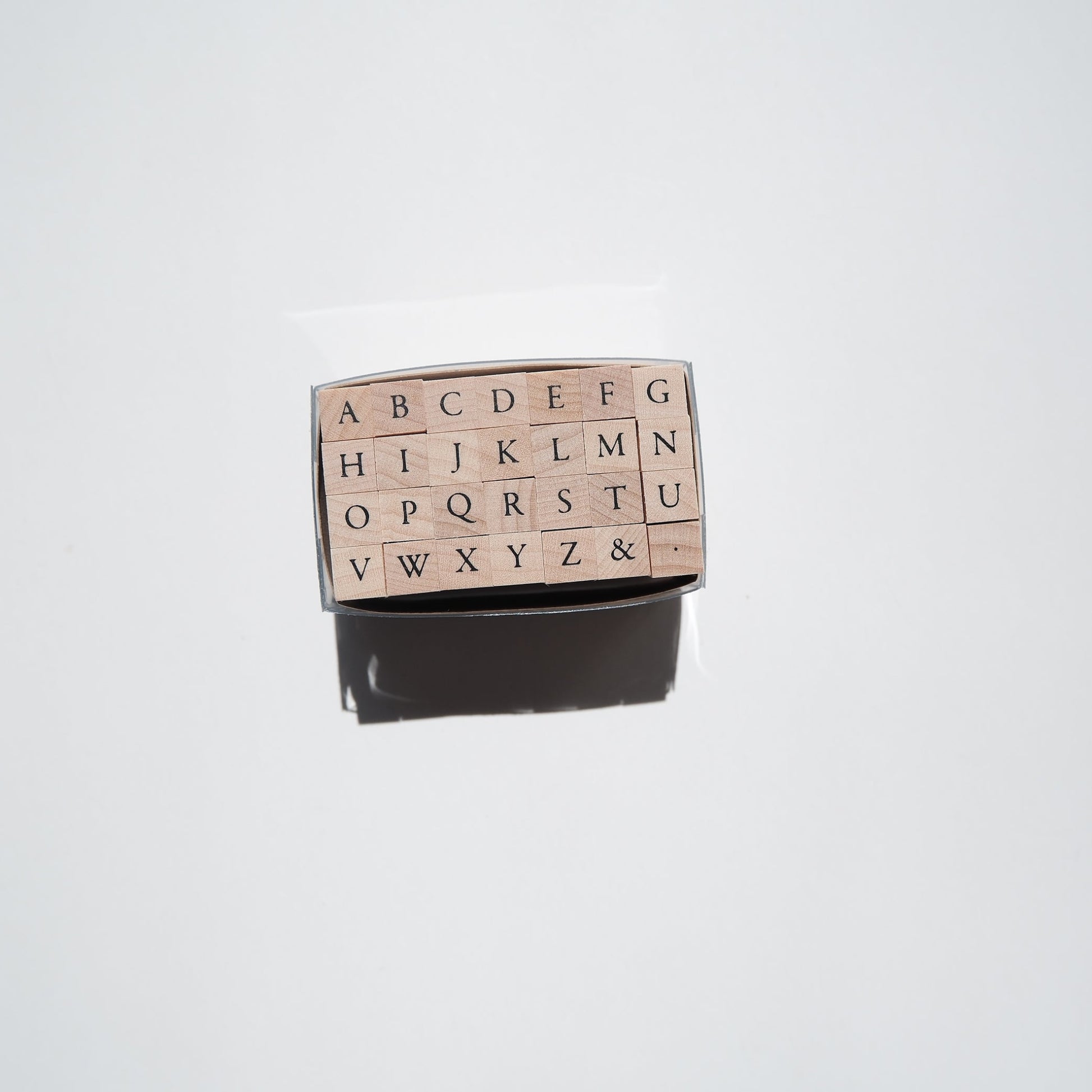 A rectangular alphabet rubber stamp with raised capital letters A through Z and punctuation marks, shown with its dark ink pad visible below on a plain light background.