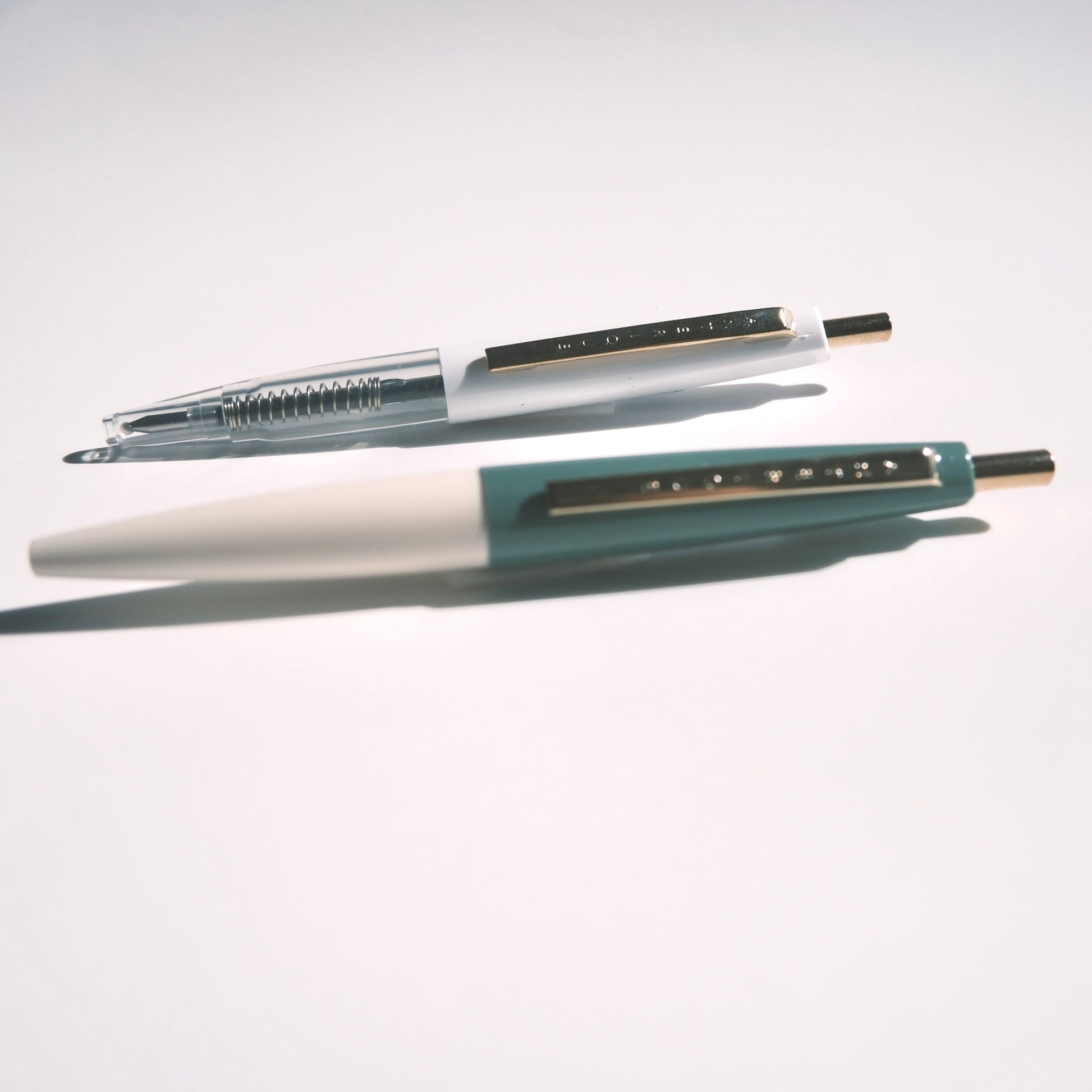 Two pens, one white and one blue, on a light gray background