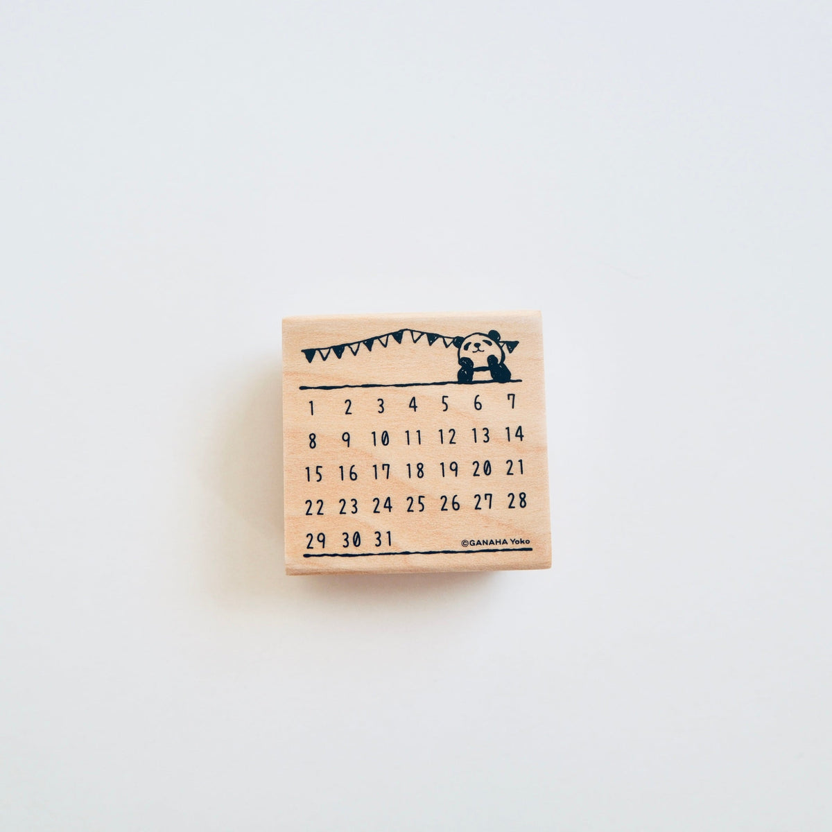 A small wooden calendar block stamp with a black printed calendar grid and bunting graphic, centered on a plain white background.