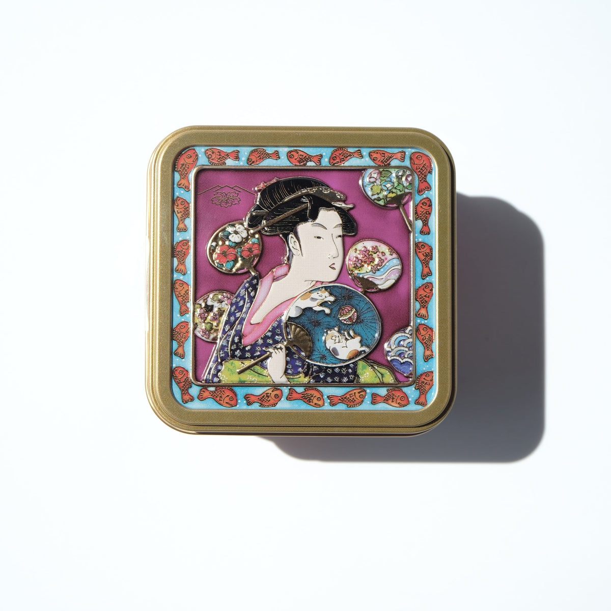 A square decorative tin with rounded corners, featuring a colorful Japanese geisha illustration on a pink background with a gold-toned border, photographed on a clean white surface with a soft shadow.