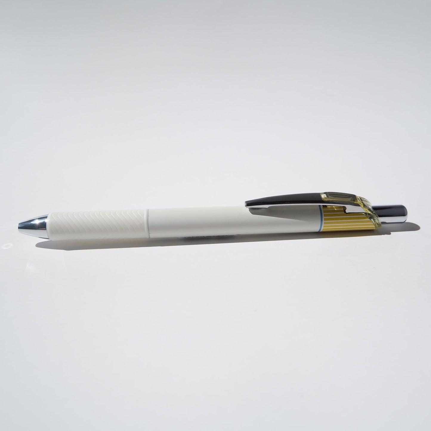 A white and yellow retractable pen with a black clip and gold accent details, resting horizontally on a plain white surface.